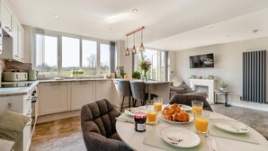 A modern kitchen with a dining area, large windows, and a view of the outdoors.