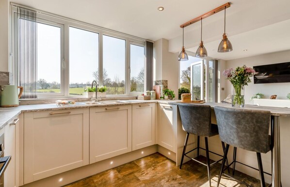 A modern kitchen with a large window, a sink, and a bar area with two chairs.