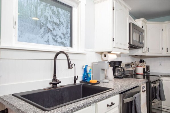 A kitchen with white cabinets, a granite countertop, a stainless steel sink, a microwave, and a coffee maker.