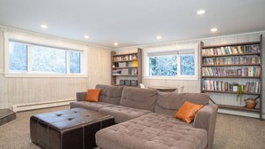 Ein modernes Wohnzimmer mit einer Eckcouch, einem Lederhocker und einem Bücherregal voller Bücher.