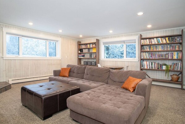 A modern living room with a sectional sofa, a leather ottoman, and a bookshelf filled with books.