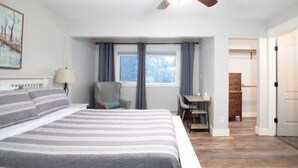 Ein Schlafzimmer mit Bett, Schreibtisch, Stuhl, Lampe und einem Fenster mit Vorhängen.