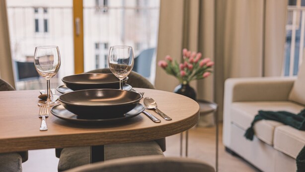 A dining table with plates, cutlery, and wine glasses set for two.