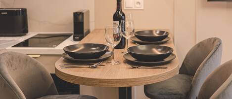 A dining table with four black plates, two wine glasses, and a bottle of wine. There are four grey upholstered chairs around the table.