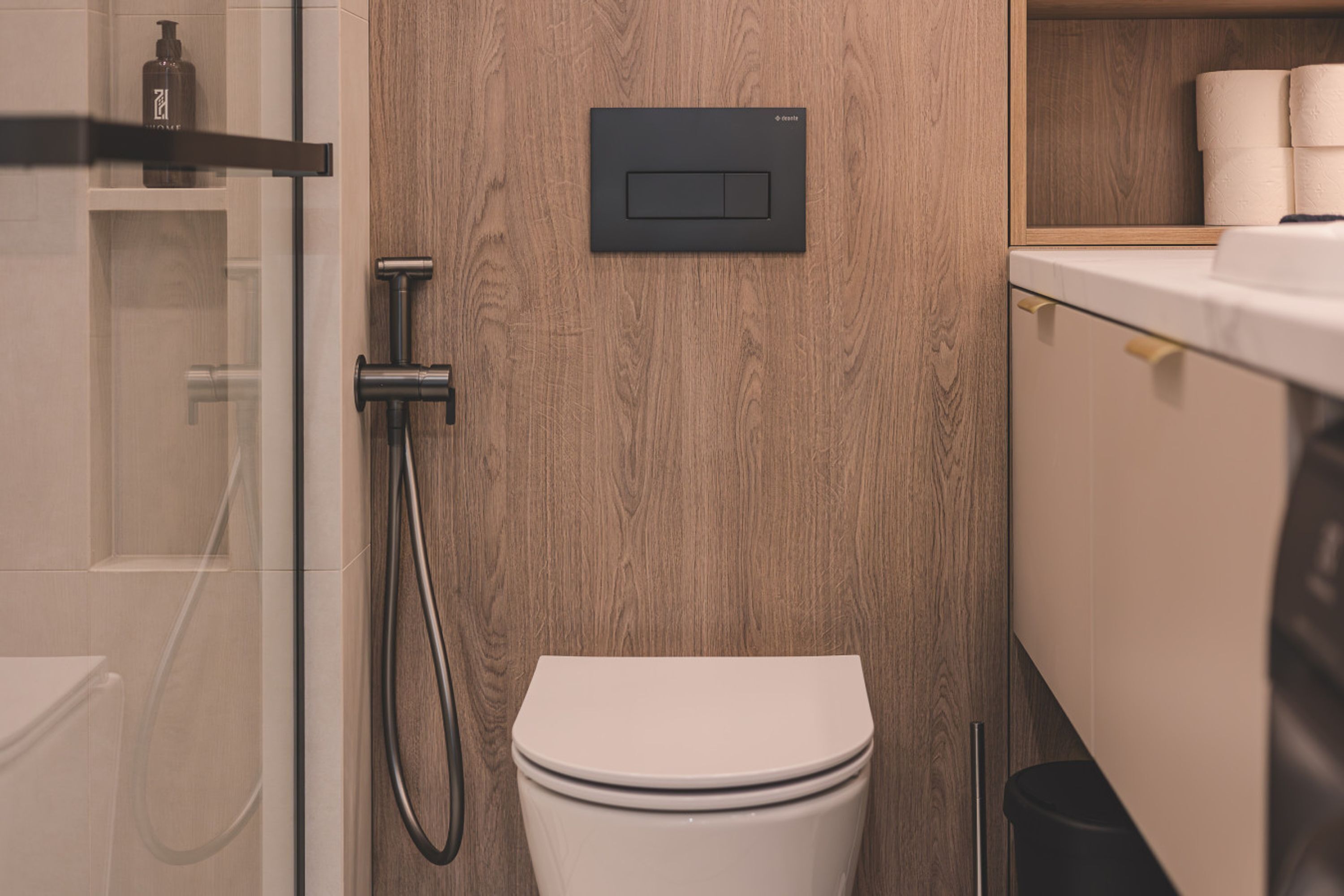 A modern bathroom with a wooden wall, a toilet, a shower, and a shelf with toiletries.
