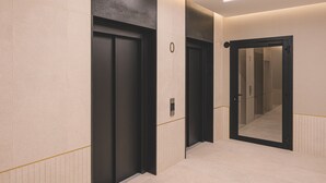 A hallway with two black doors, one with a visible elevator control panel, and a mirrored wall reflecting the hallway.
