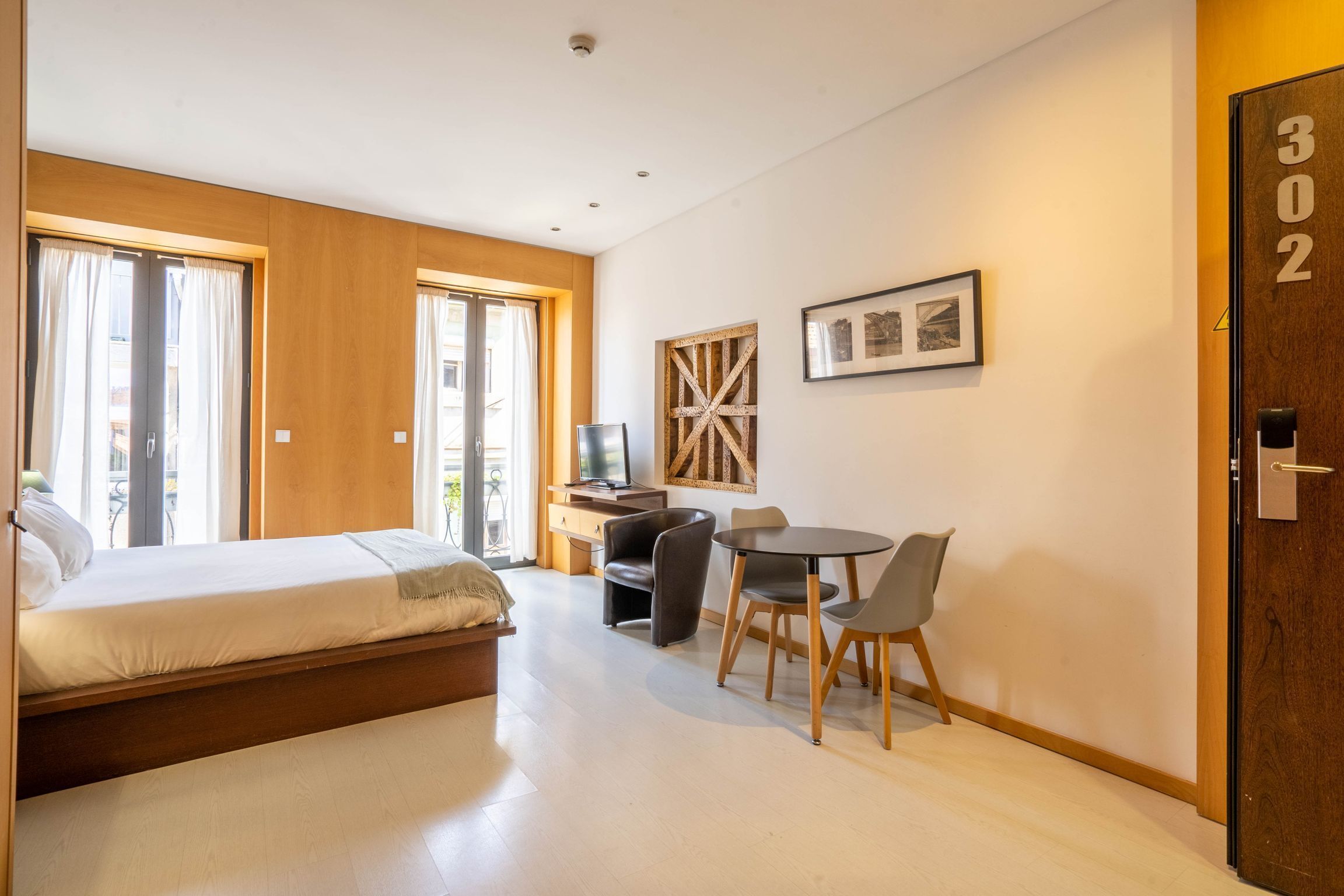 Une chambre d’hôtel moderne équipée d’un lit, d’un bureau avec une chaise, d’une télévision et d’une grande fenêtre.