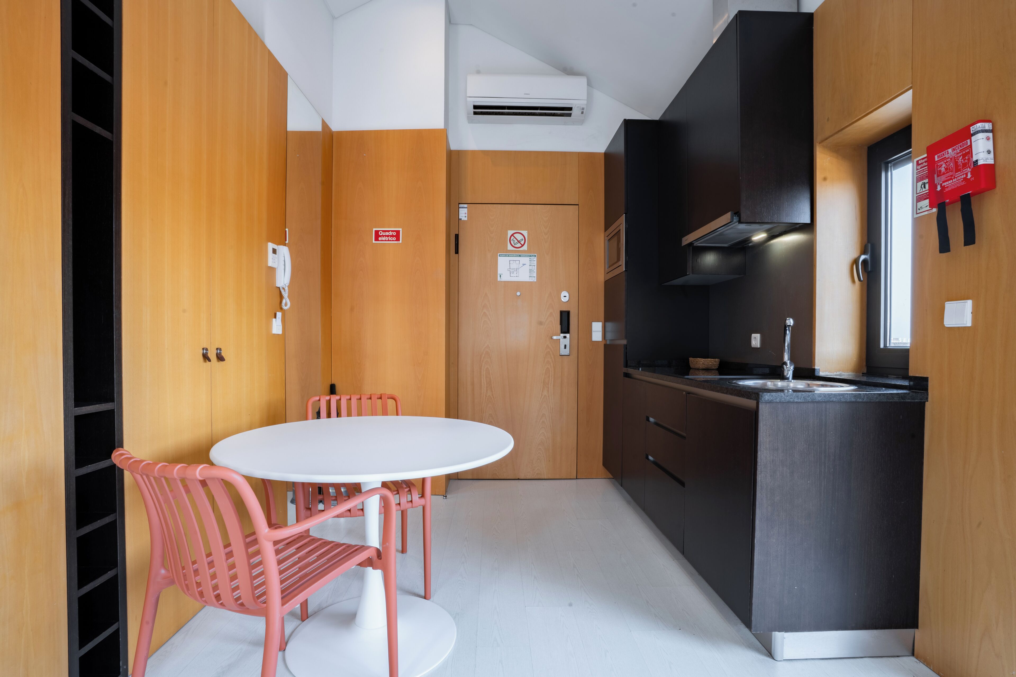 Una cocina moderna con una mesa blanca y sillas rosadas, paredes de madera y un armario negro.