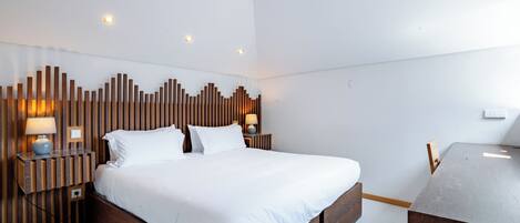 Une chambre d’hôtel moderne avec un grand lit, une tête de lit en bois, des lampes de chevet et un bureau en bois.