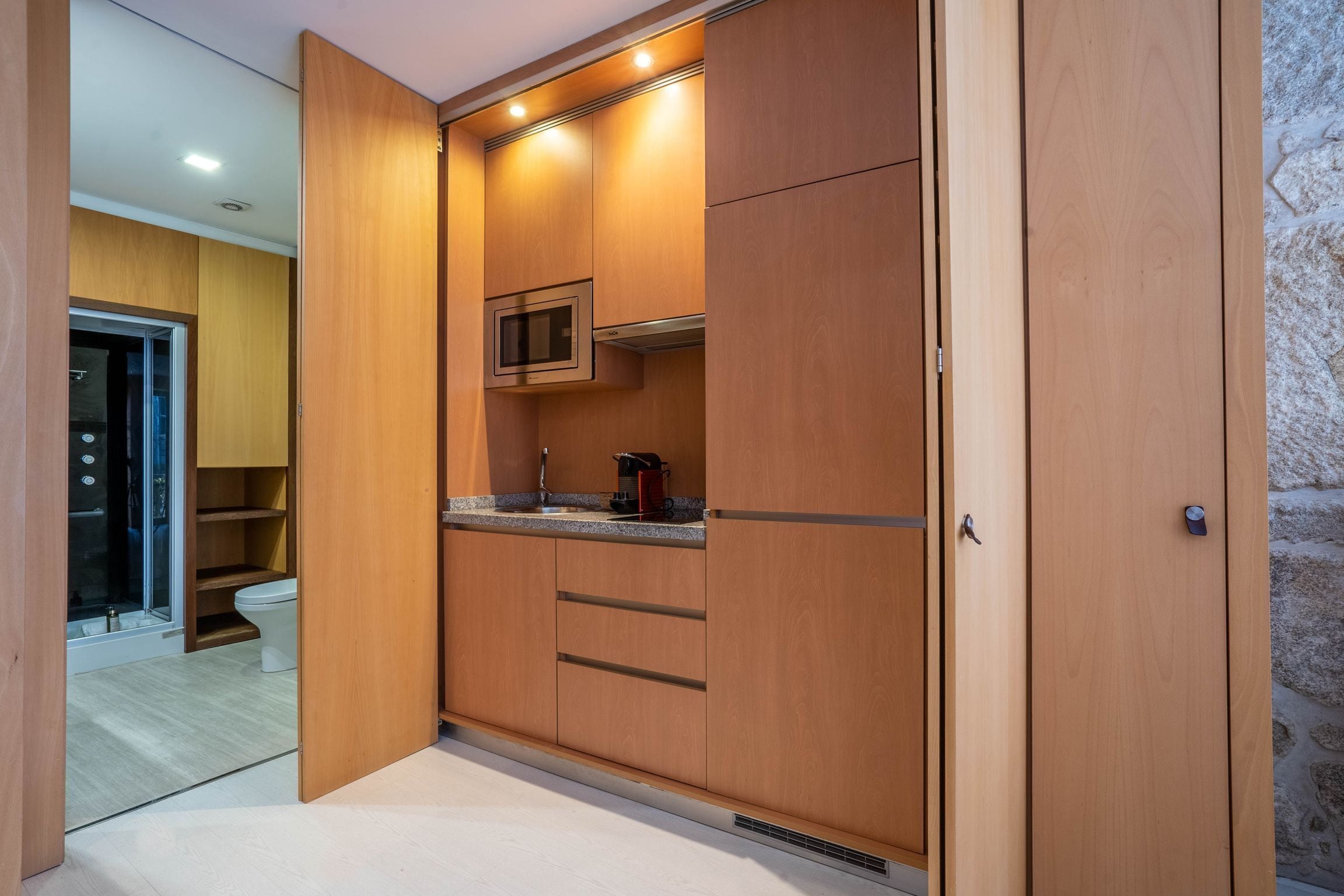 A modern kitchen with wooden cabinets, a microwave, and a coffee machine.