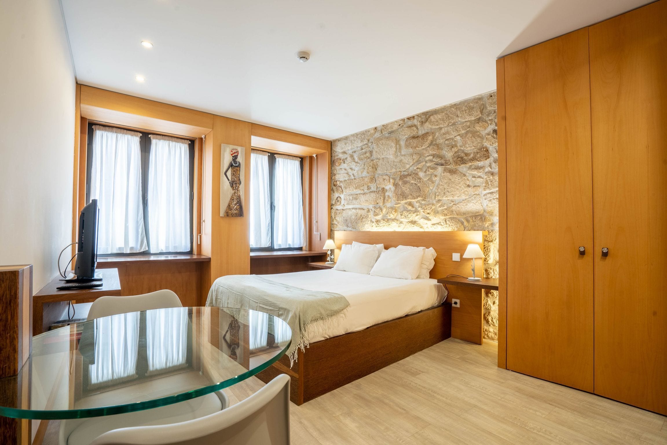 A bedroom with a bed, a desk, a glass table, and a wardrobe.