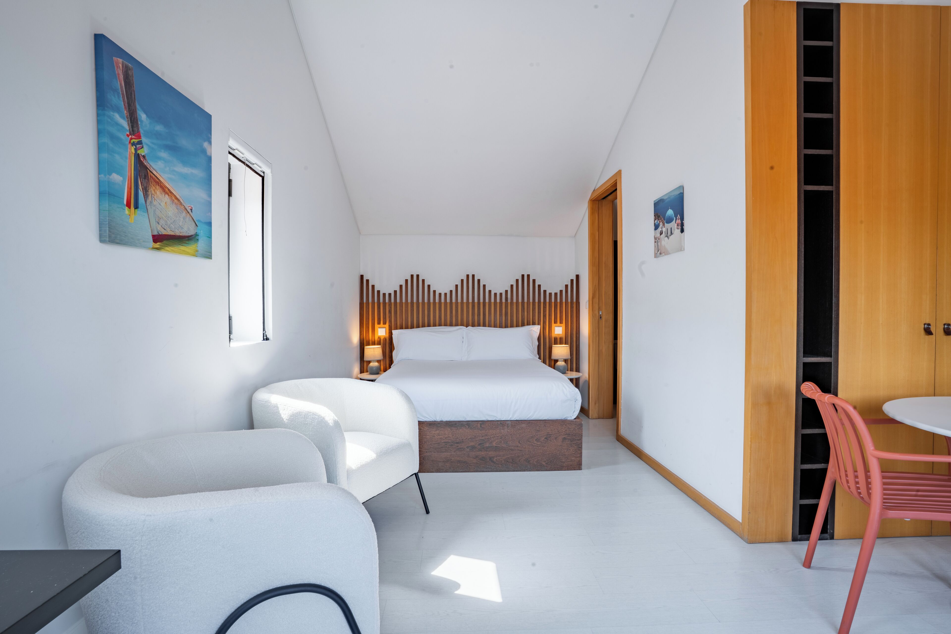 Ein modernes Hotelzimmer mit einem Bett, zwei Nachttischen, einem Sessel, einem kleinen Tisch und einem Holzschrank.