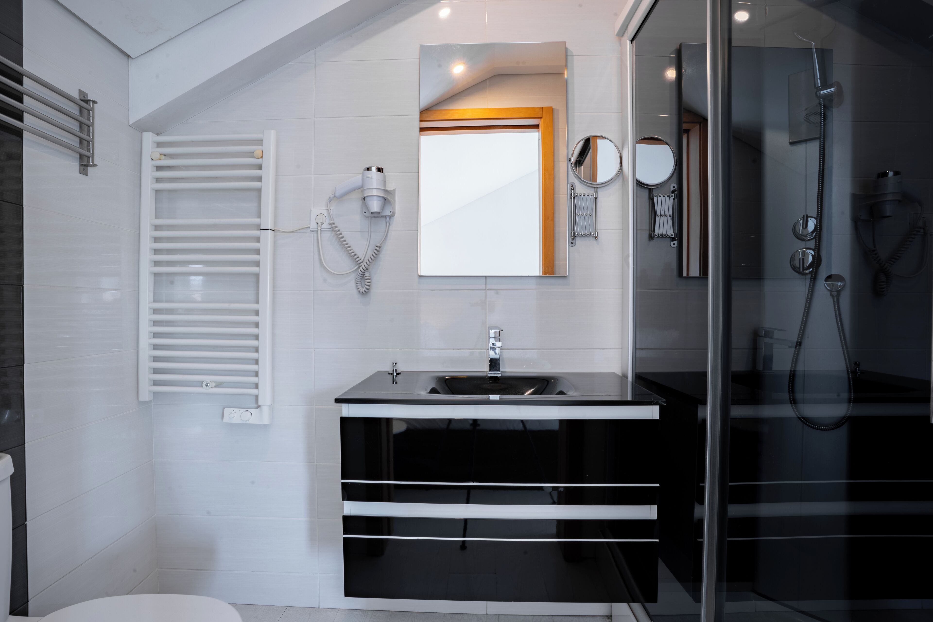 Une salle de bain moderne dotée d’une douche à parois de verre, d’un porte-serviettes blanc, d’un grand miroir et d’un meuble-lavabo noir.