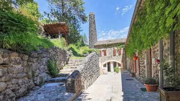 Un estrecho callejón adoquinado con paredes de piedra, una escalera de piedra y un edificio con techo de tejas y arco de entrada.