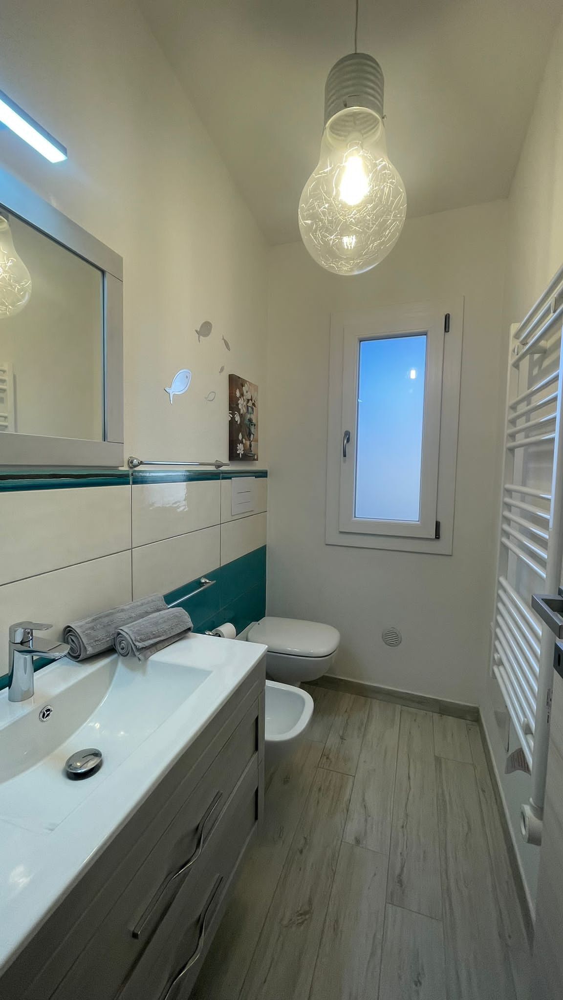 Een moderne badkamer met een wit wastafelmeubel, toilet en raam.