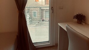 A room with a sliding glass door, a white desk, a small potted plant, and a view of a building outside.