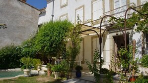 Un cortile con piscina, piante in vaso e una pergola.