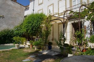 Un patio con piscina, plantas en macetas y una pérgola.