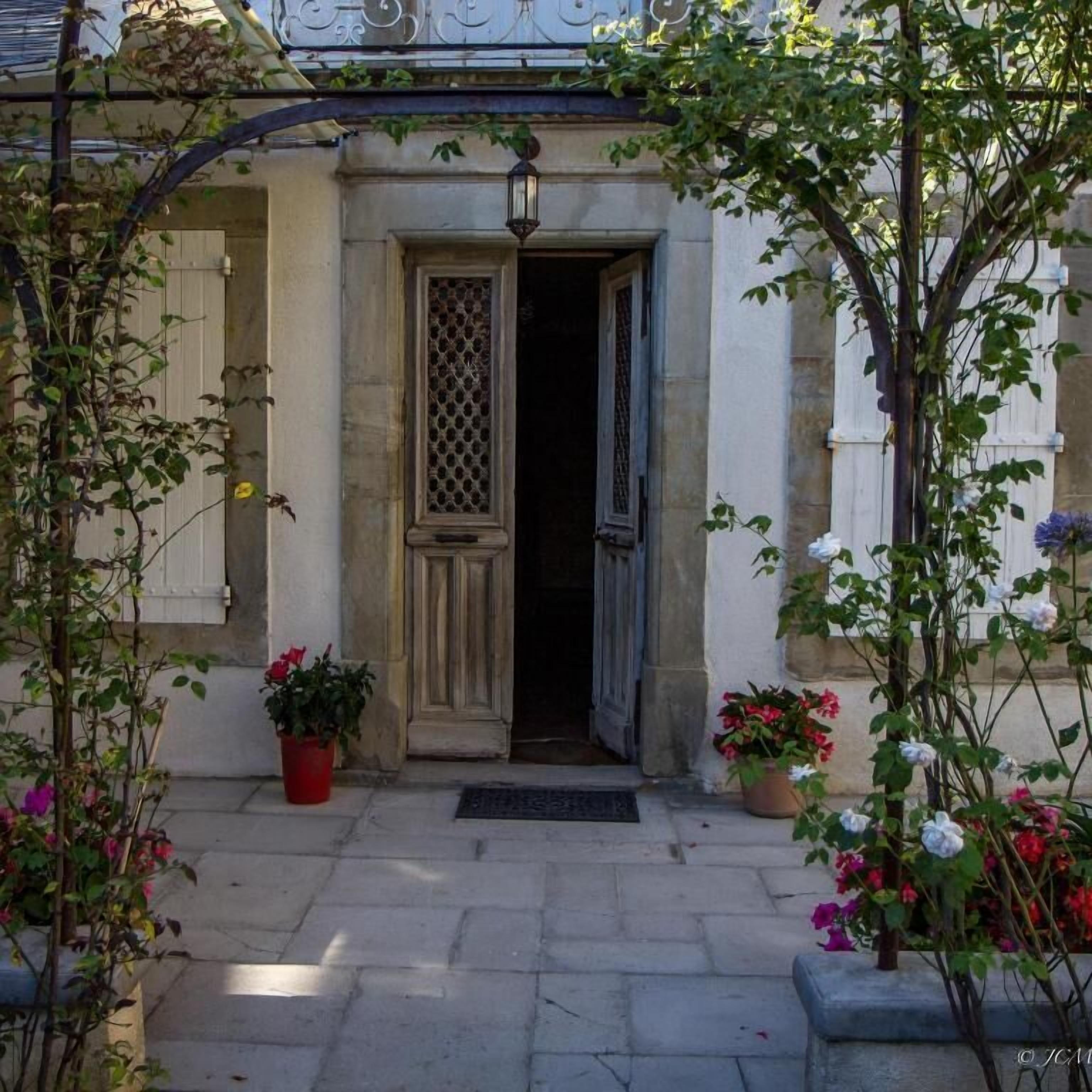 Un edificio in pietra con una porta in legno, piante in vaso e un arco in metallo.