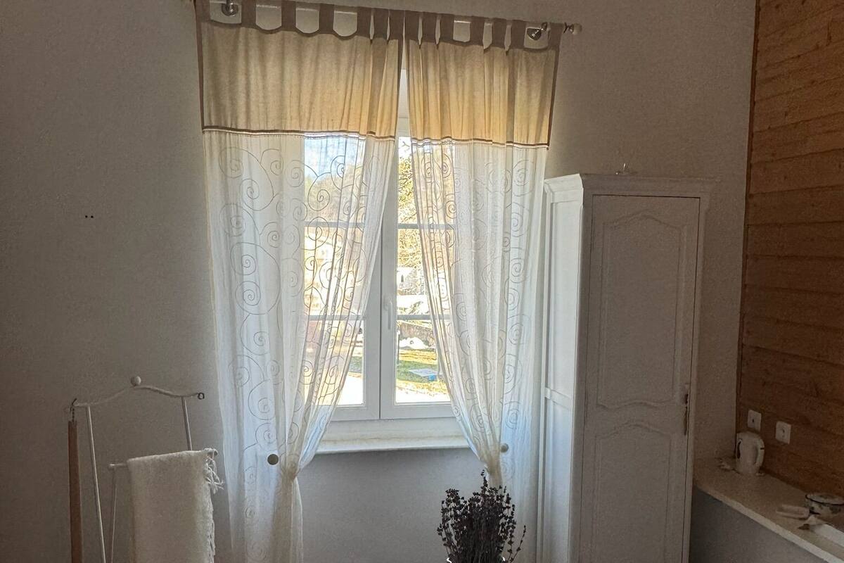 Una habitación con ventana, una mesa blanca con un florero y dos sillas blancas.