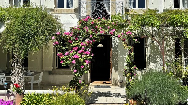 Un edificio con ingresso affacciato su un giardino, un cancello in metallo e un vialetto che conduce alla porta.