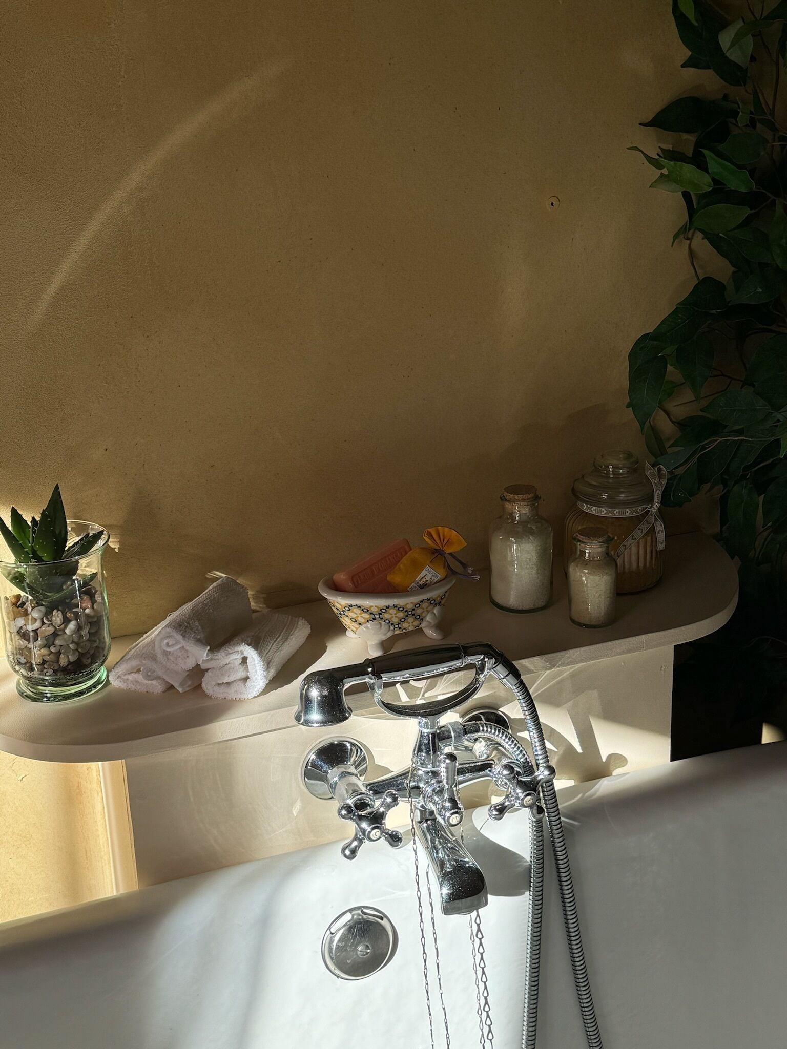 A bathroom with a bathtub, a glass jar with pebbles, a towel, and a plant.