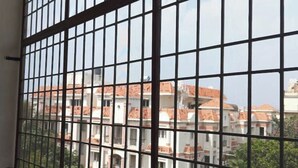 Vista attraverso una finestra con sbarre di metallo, che mostra una zona residenziale con diversi edifici e cielo sereno.