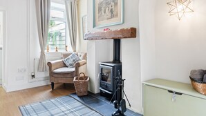 Un salon chaleureux avec une cheminée, un fauteuil confortable, un panier en osier et un luminaire suspendu en forme d’étoile.