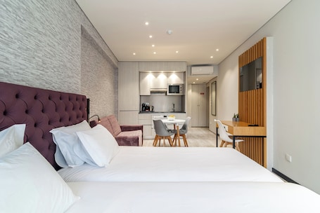 A modern hotel room with a large bed, a dining area, and a kitchenette.