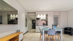 A modern kitchen with built-in appliances, a dining area with a glass table and chairs, and a black leather chair in the corner. - Smartr Porto Gaia & Spa (Vila Nova de Gaia)