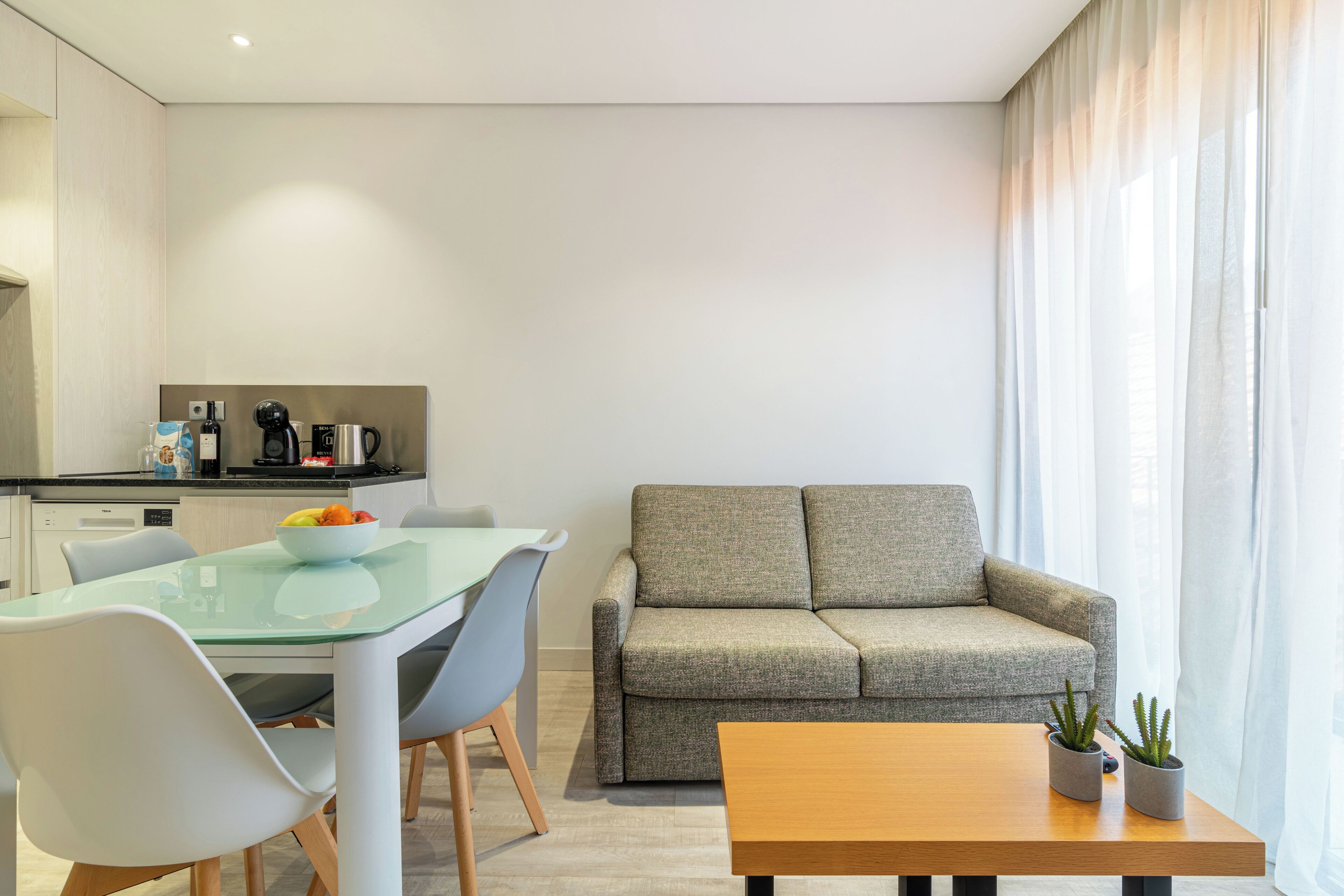 A modern living room with a glass dining table, grey sofa, and a wooden coffee table.