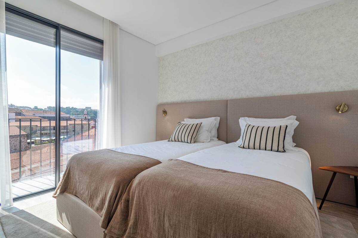 Quarto de hotel com duas camas, uma janela grande e vista para a cidade.