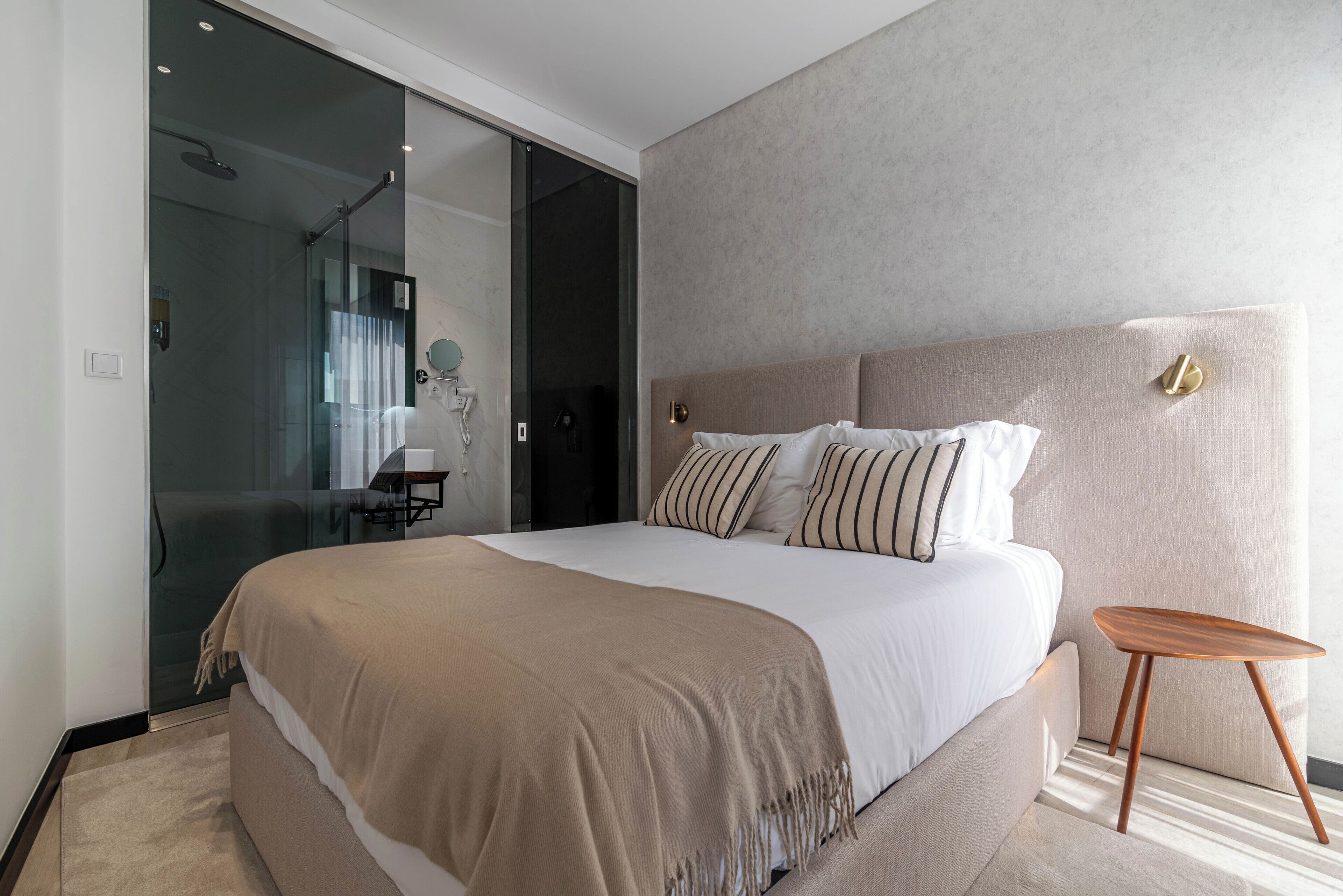 Une chambre à coucher moderne avec un grand lit, une cabine de douche en verre et une petite table de chevet en bois.
