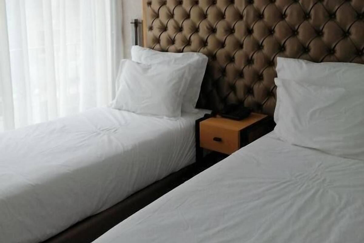 Quarto de hotel com duas camas, cabeceira estofada, roupa de cama branca e uma mesa de cabeceira.