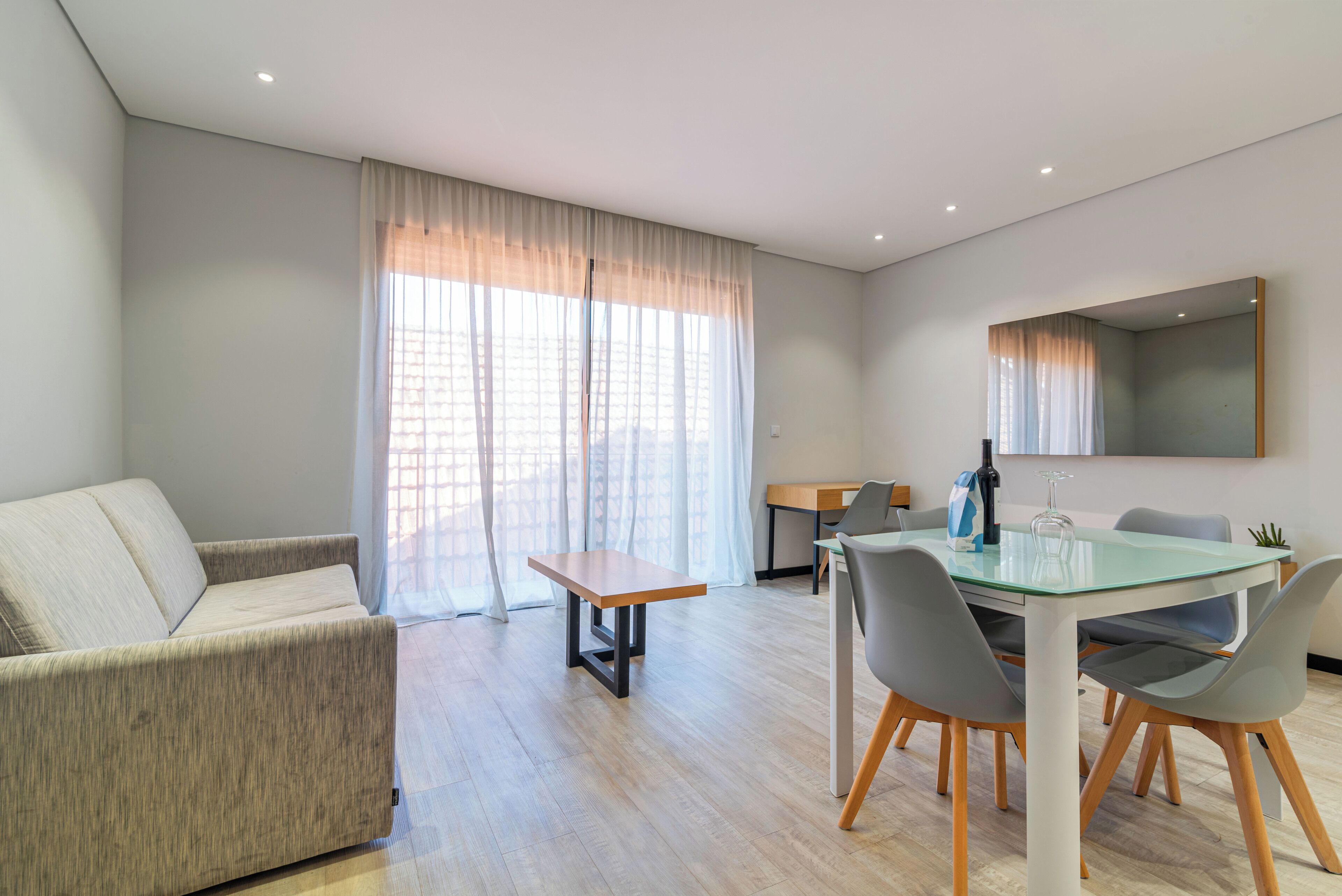 Una sala moderna con un sofá, una mesa de vidrio para comer y una pequeña mesa de madera.
