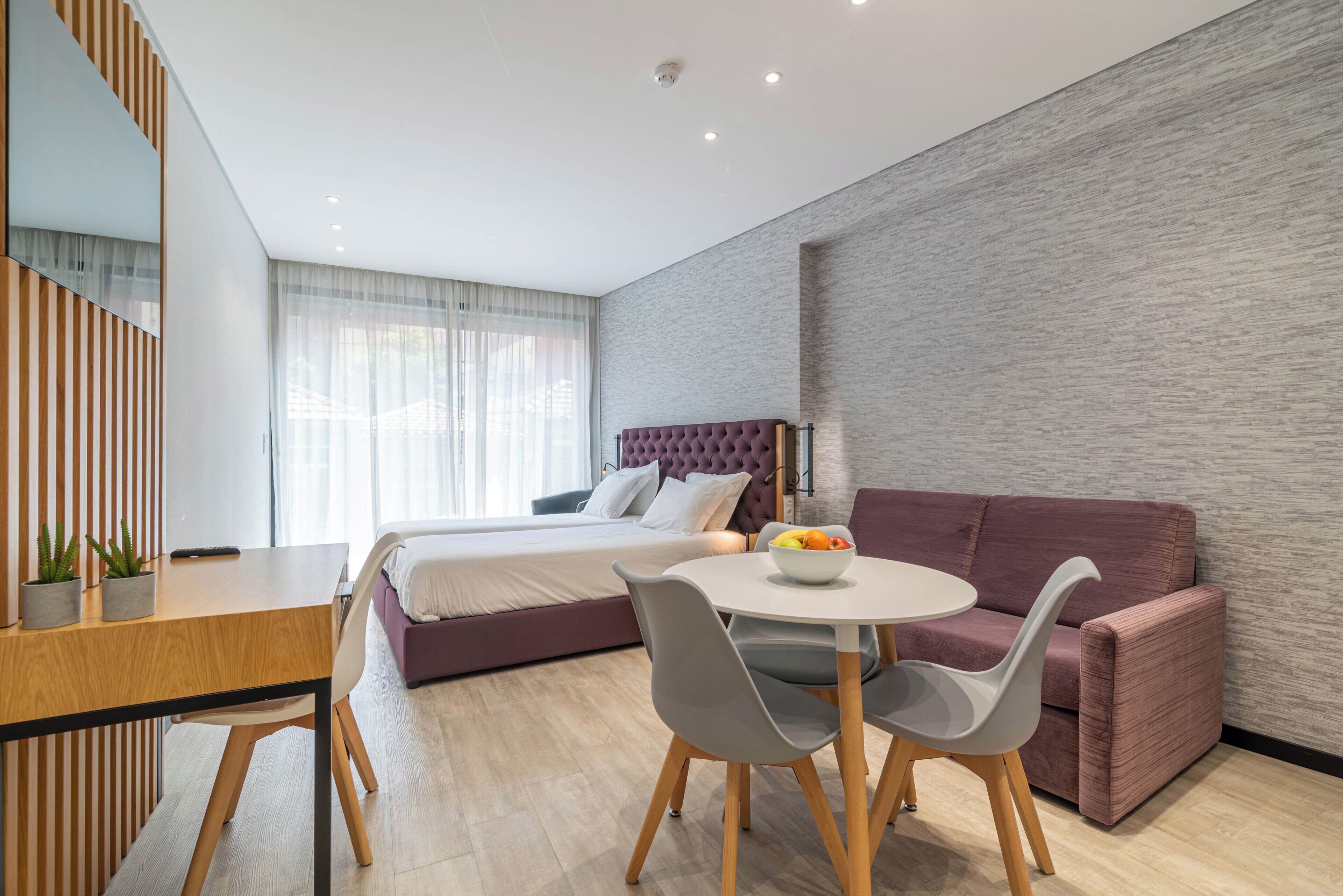A modern bedroom with a bed, a dining table with chairs, a sofa, and a small table with fruit.