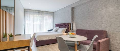 A modern bedroom with a bed, a dining table with chairs, a sofa, and a small table with fruit.