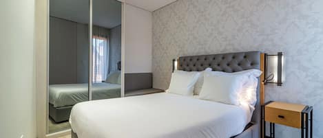 A modern hotel room with a large bed, a bedside table, and a sliding door closet.