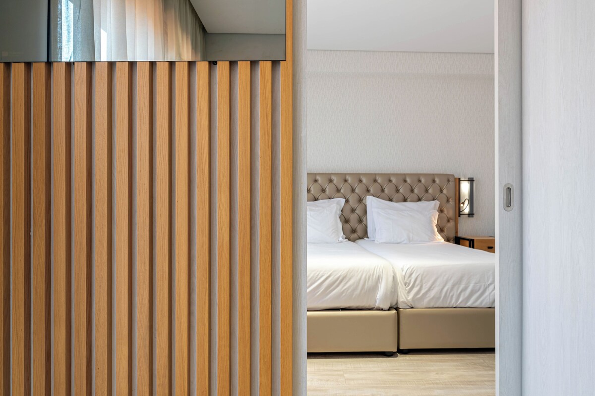 A modern bedroom with a large bed, a wooden slat partition, and a neutral color scheme.
