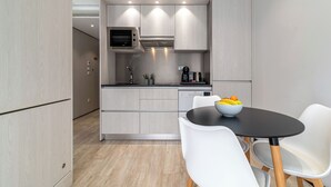 A modern kitchen with built-in appliances, a dining area with a black table and white chairs, and a bowl of fruit on the table. - Smartr Porto Gaia & Spa (Vila Nova de Gaia)
