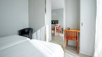 Een moderne hotelkamer met een groot bed, een bureau en een stoel. Achterin is een kitchenette te zien.