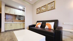 A modern living room with a black leather sofa, a white coffee table, and a kitchen area with light-colored cabinets and a tiled backsplash. - Zhu Youjia Homestay (Chongqing)