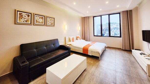 A modern hotel room with a black leather sofa, a white bedside table, a bed with an orange runner, a large window with a city view, and three framed floral artworks on the wall. - Zhu Youjia Homestay (Chongqing)