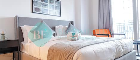 A neatly made bed with a grey headboard, a framed artwork above it, and a view of a balcony through a window.