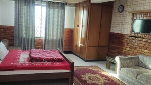 Un dormitorio con cama, armario, televisor montado en la pared y sofá.