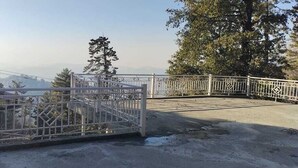 Una entrada protegida por una reja de metal, un sendero de concreto y árboles al fondo.