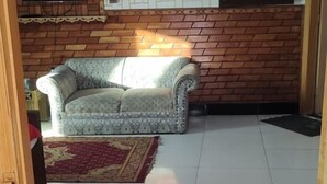 Una sala de estar con un sofá, un televisor montado en una pared de ladrillo y una alfombra estampada en el suelo.