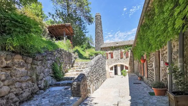 Un estrecho callejón adoquinado con paredes de piedra, una escalera de piedra y un edificio con techo de tejas y arco de entrada.