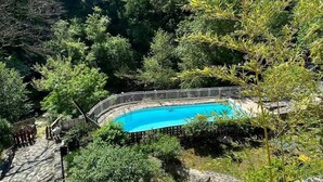 Una piscina rodeada de un bosque frondoso, con una terraza de madera y una valla blanca.