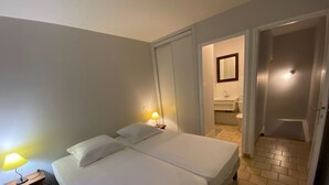 Habitación de hotel con dos camas, una mesita de noche, una lámpara y un baño visible a través de una puerta abierta.